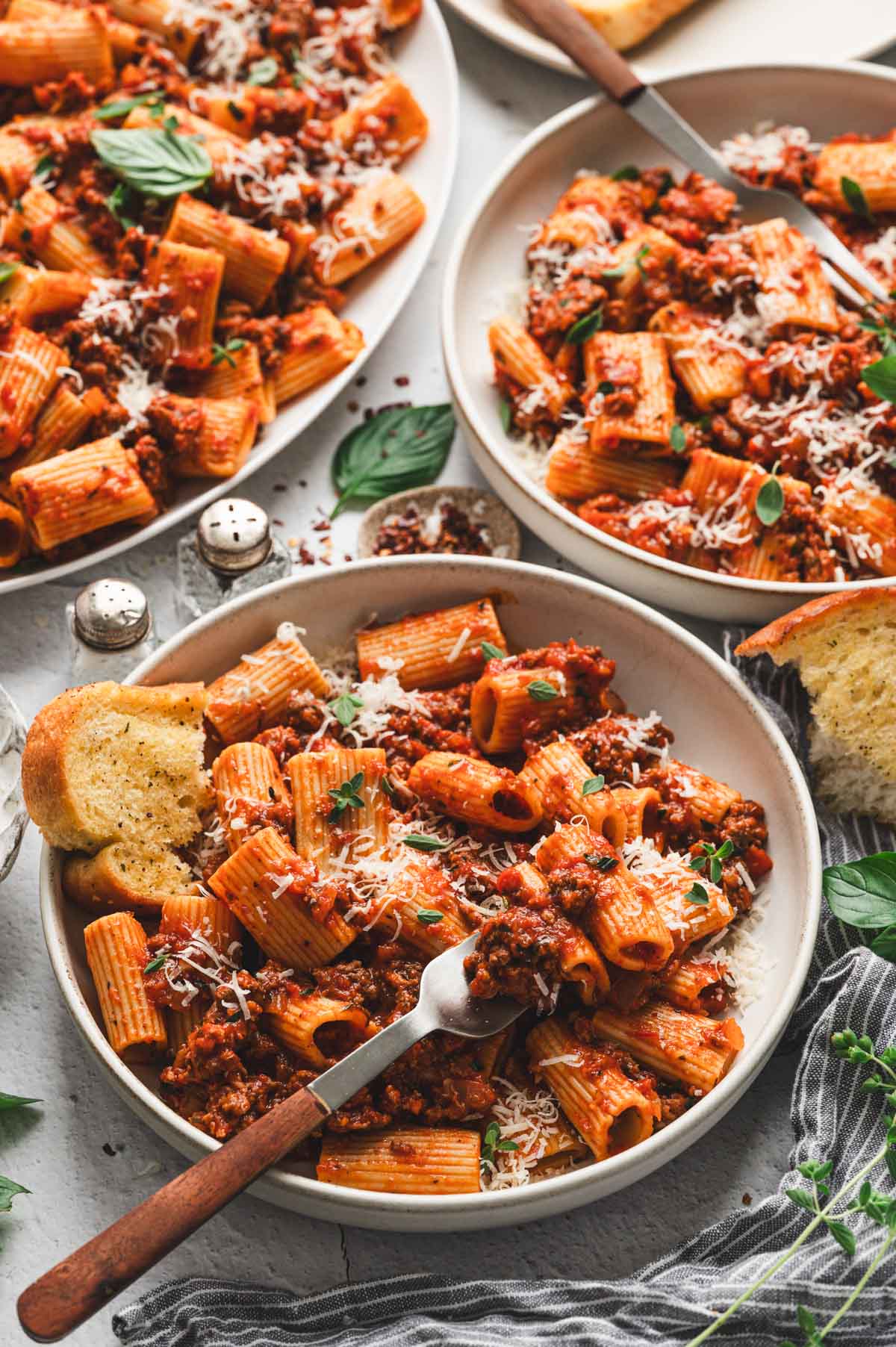 Rigatoni bolognese on a white plate with fork and garlic bread.