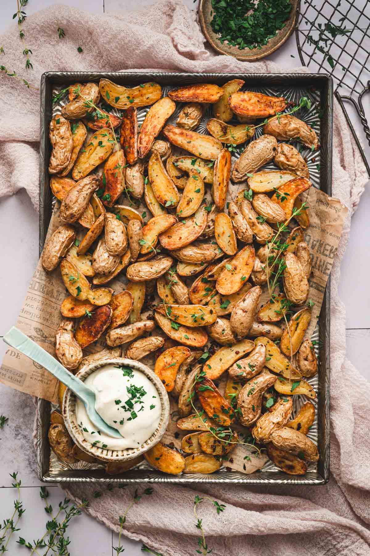 Roasted fingerling potatoes sliced in half on a baking sheet lined with parchment paper and a small bowl with a white dipping sauce inside.