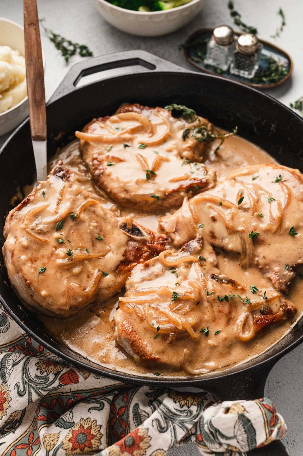 Smothered pork chops with sauteed onions and creamy white wine sauce in a cast iron pan.