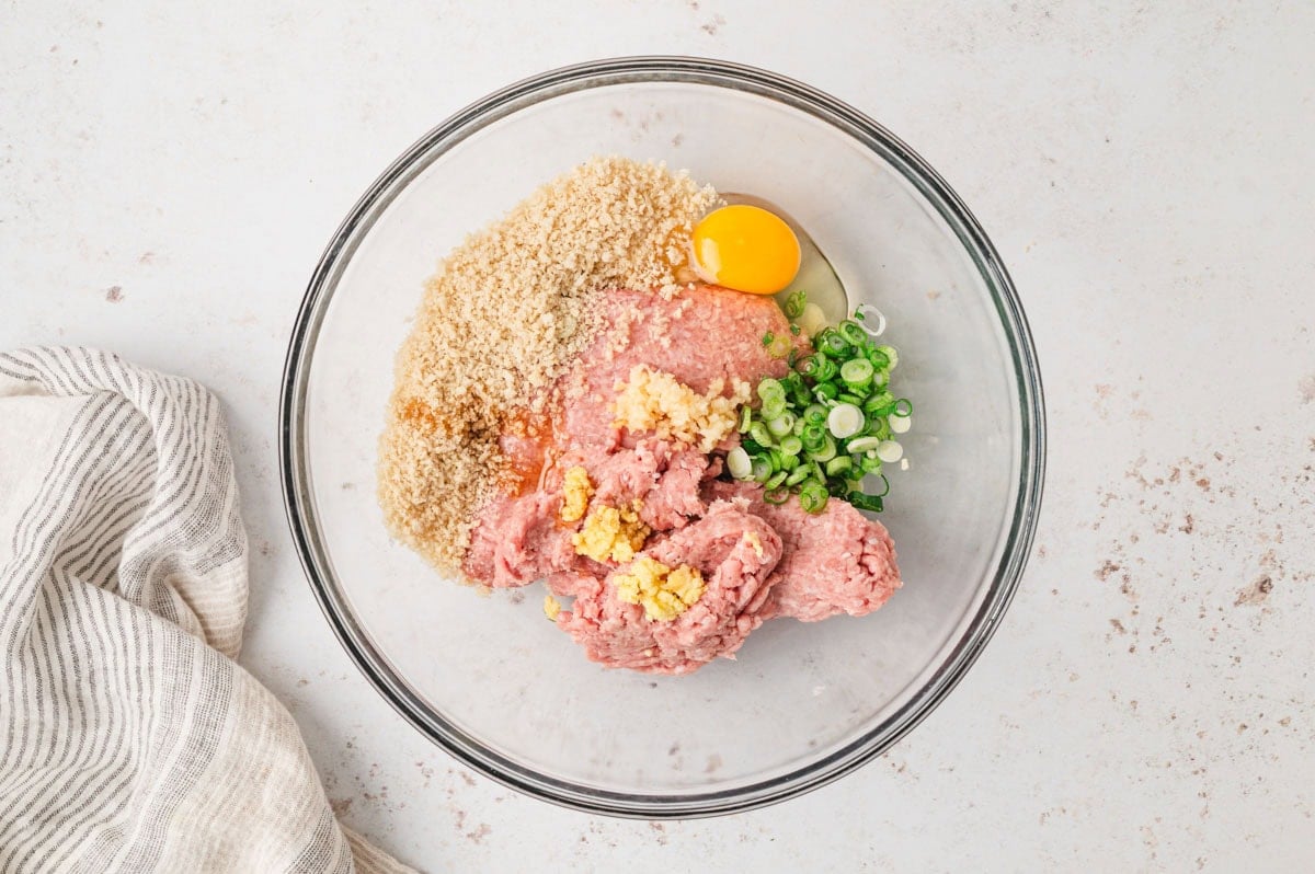 Ground turkey, breadcrumbs, green onions, egg, sesame oil, ginger, and garlic in a clear glass bowl.