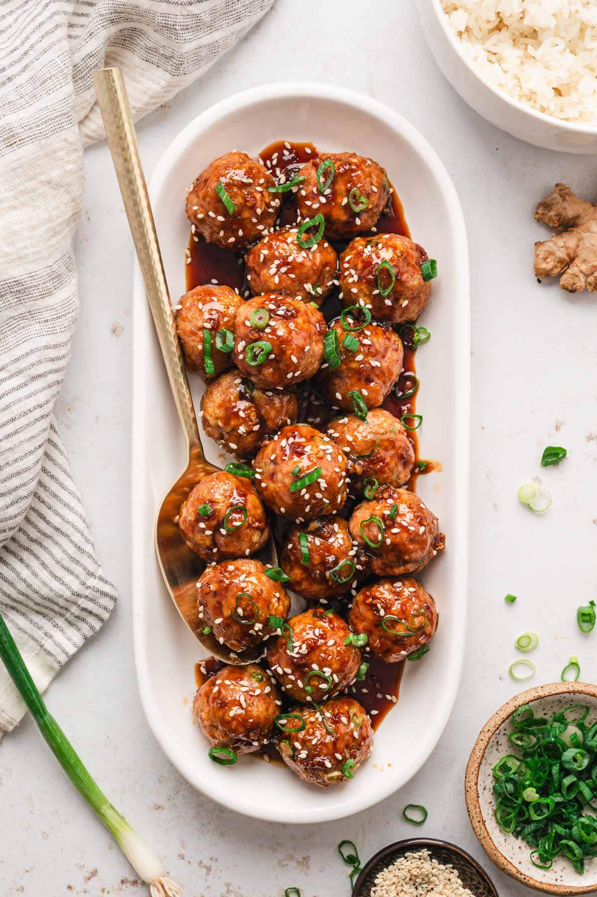Teriyaki glazed meatballs on a white platter garnished with sesame seeds and green onions.