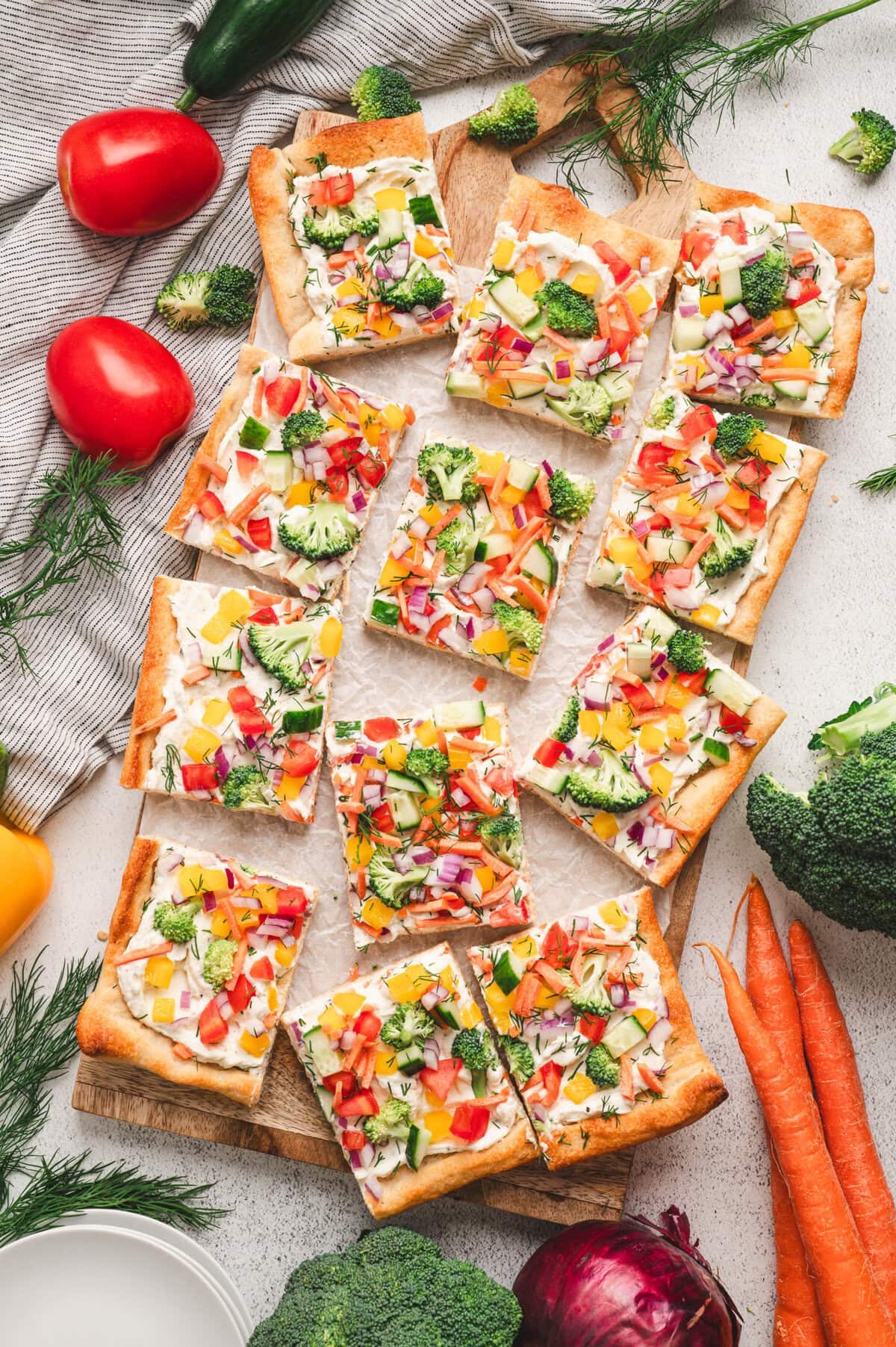 Veggie pizza cut up into pieces on a wooden board with veggies surrounding the pizza.