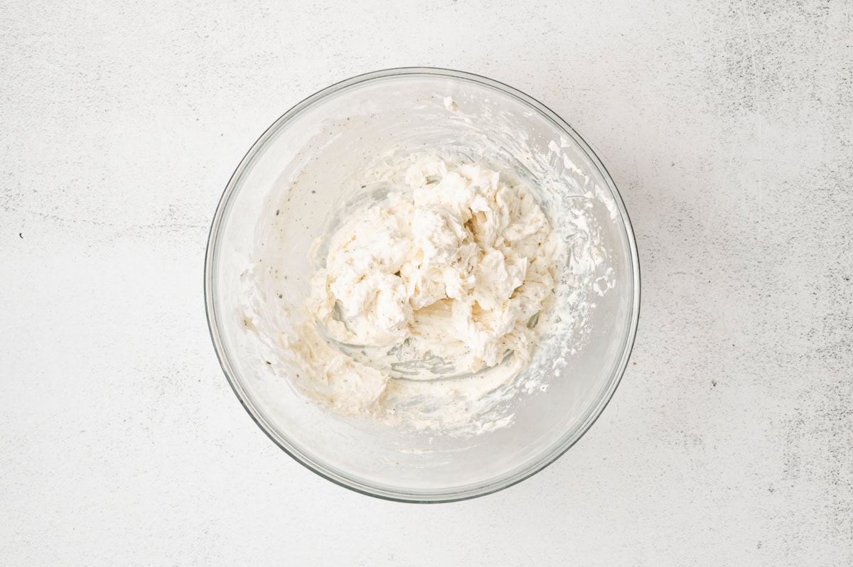 Cream cheese, sour cream, and seasonings mixed together in a glass bowl.