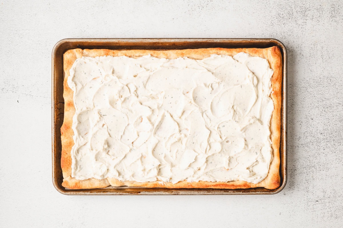 Baked pizza dough spread with cream cheese mixture on a sheet pan.