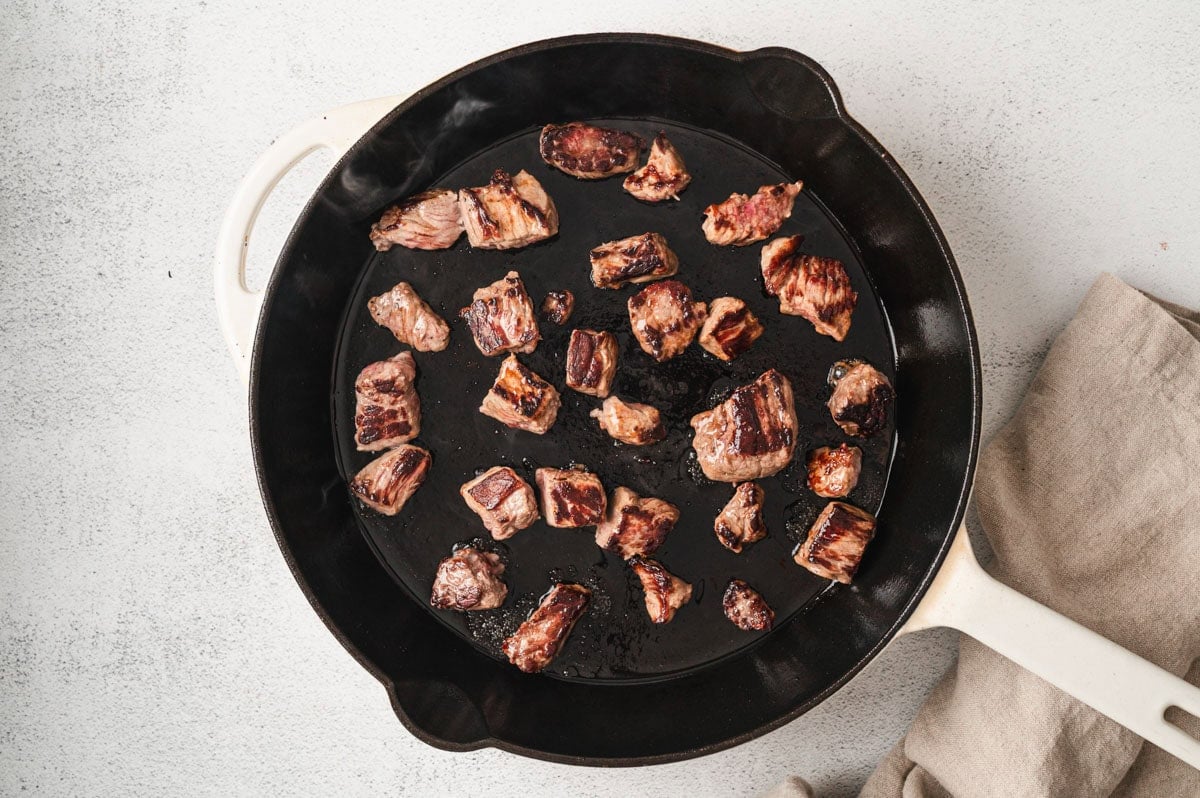 Beef chunks being browned in a cast iron skillet.