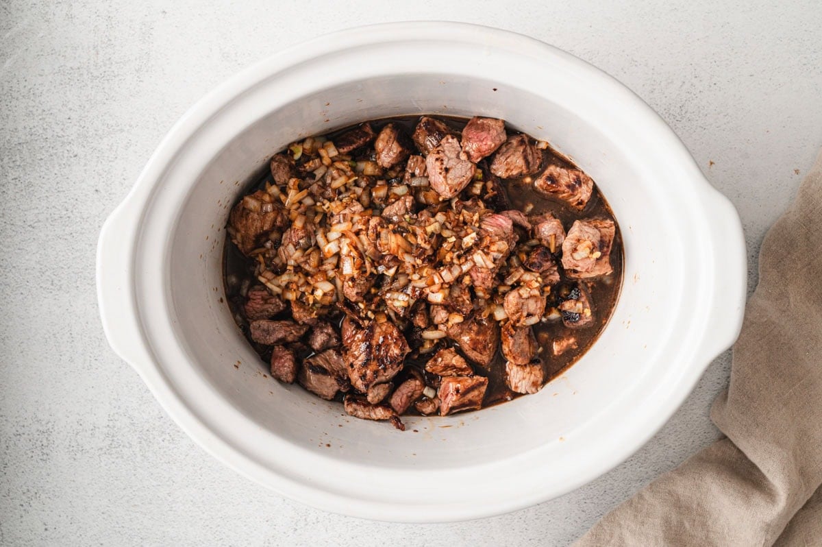 White crockpot with beef, onions, garlic for Crockpot Beef and Noodles.