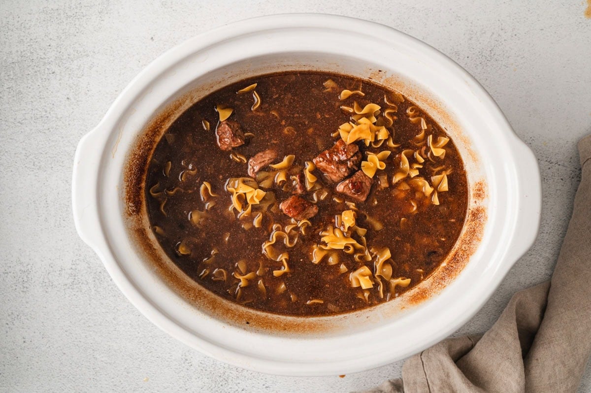Fully cooked beef and noodles in sauce in a white crockpot.