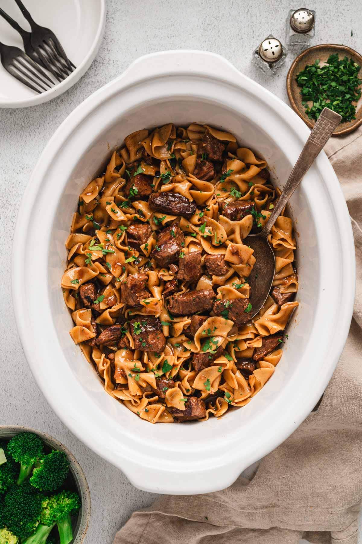 Beef and noodles in a white crockpot with a serving spoon.