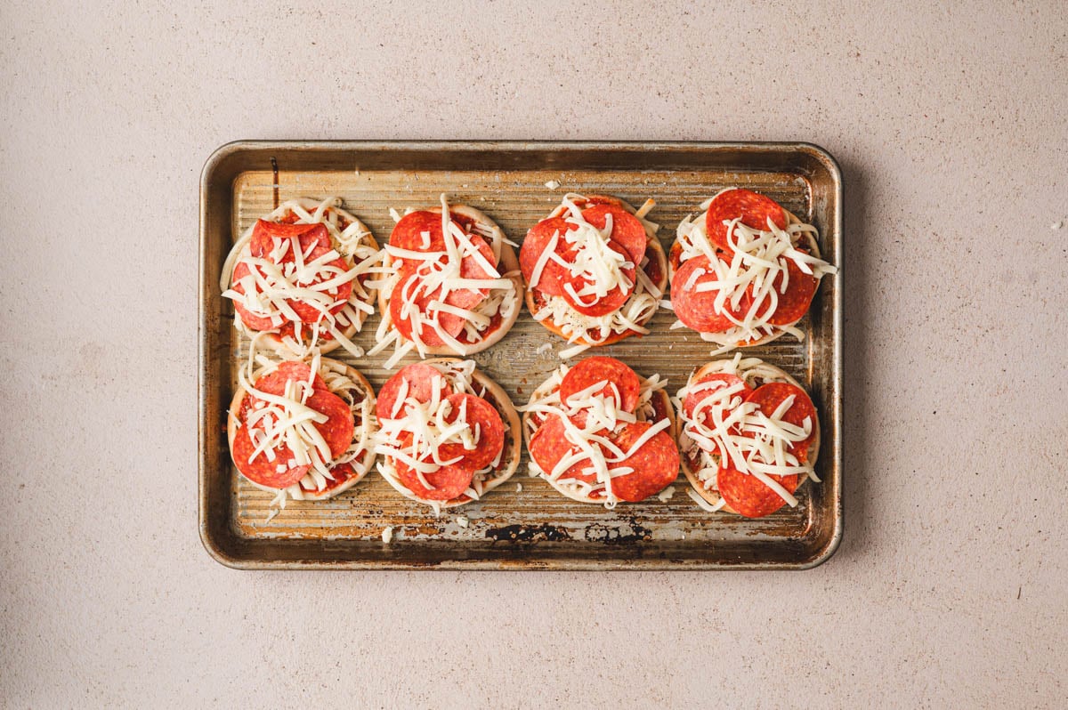 English muffins on a sheet pan with sauce, cheese, and pepperoni.