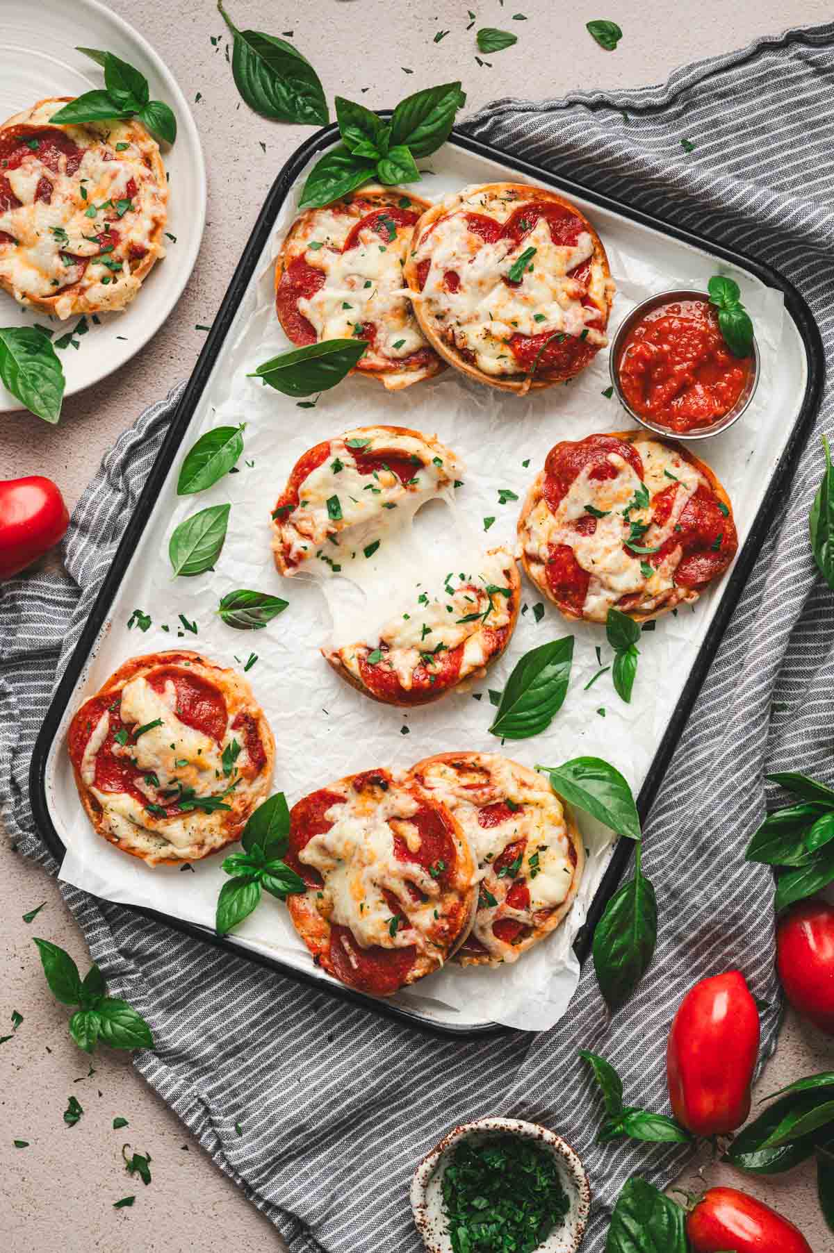 English muffin pizzas topped with cheese, pepperoni, and fresh basil.