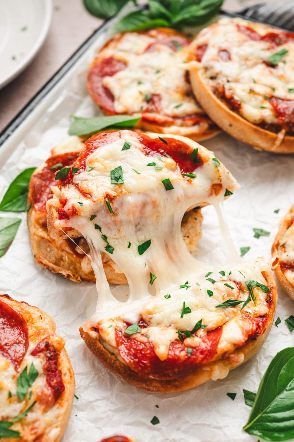 close up of english muffin pizzas with melty cheese and fresh basil.