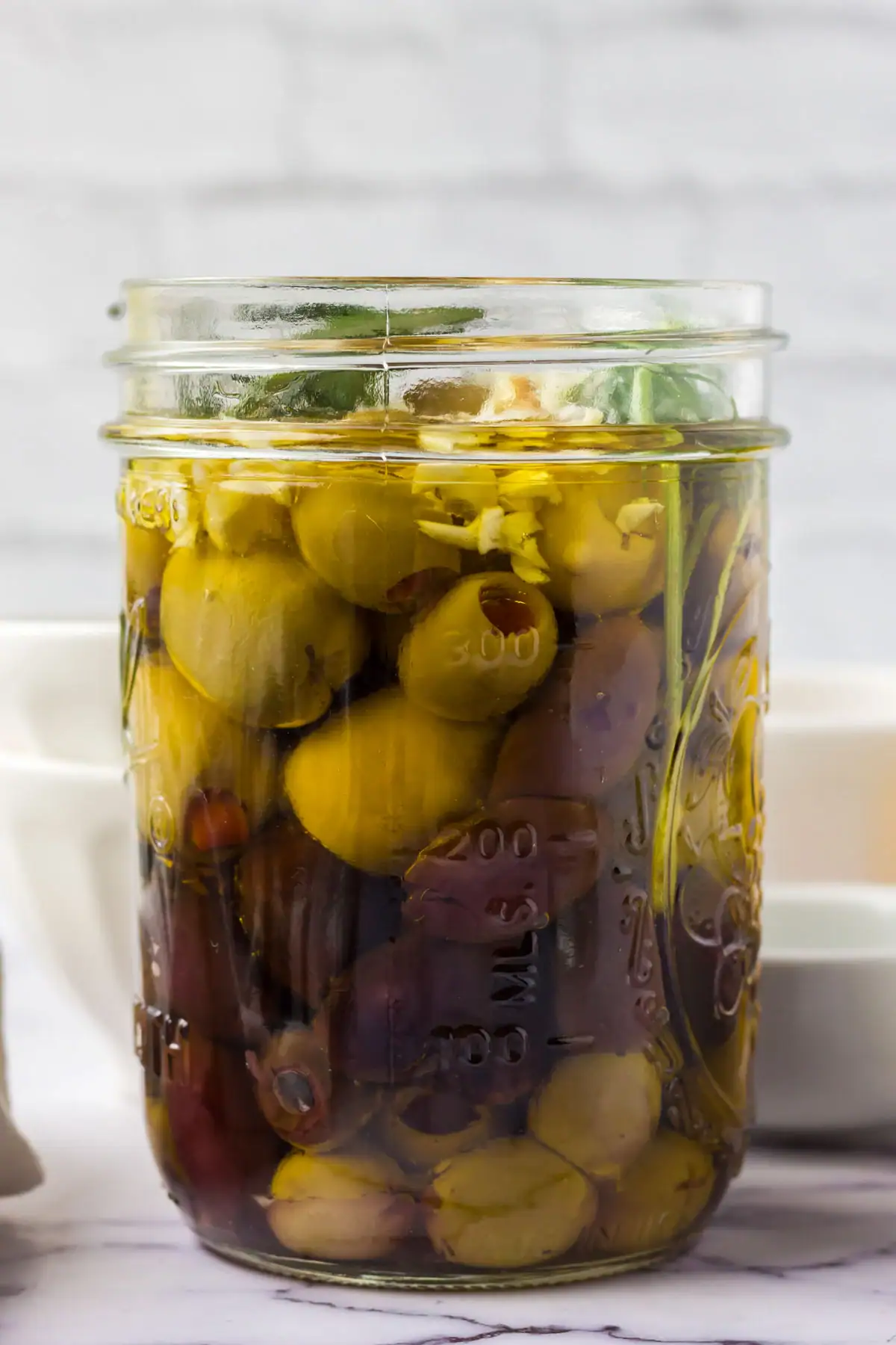 Jar of olives with herbs, garlic, and olive oil.