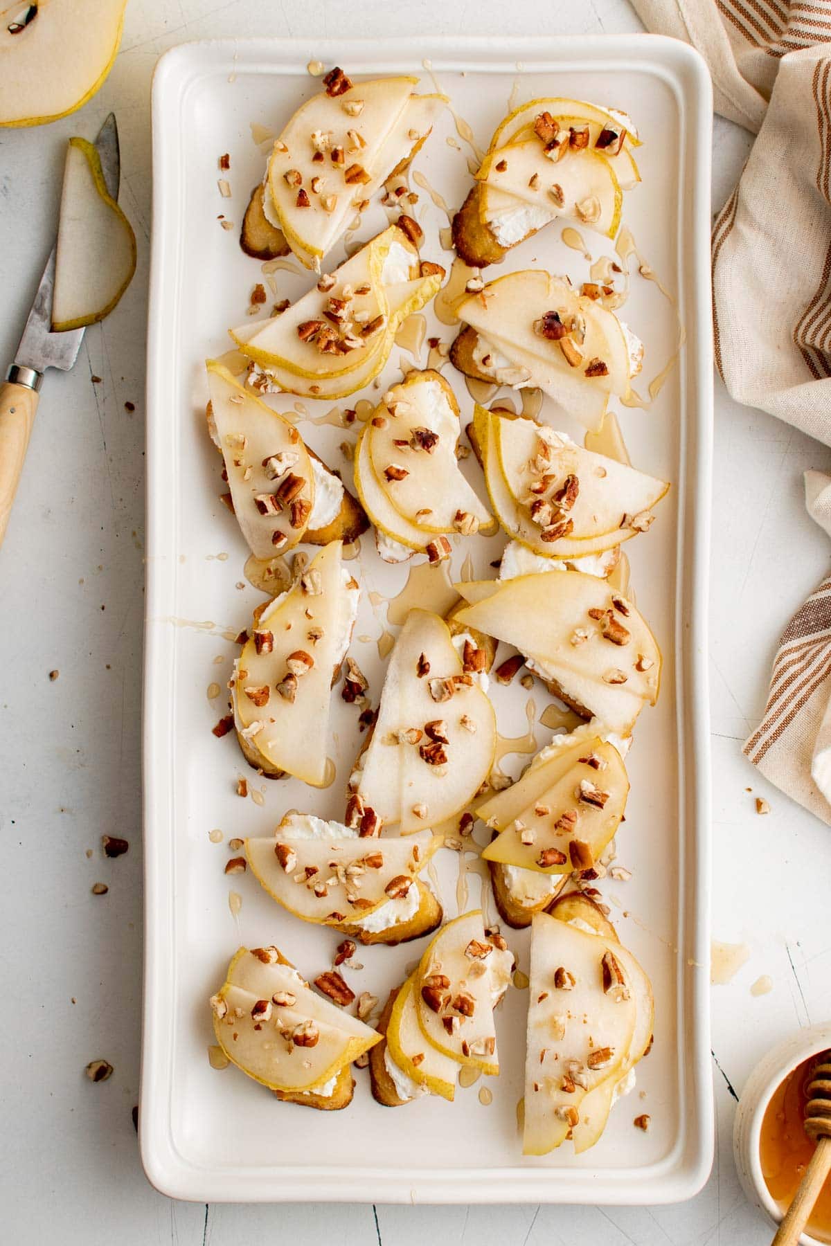 White platter with appetizers made with toasted crostini, goat cheese and pears.