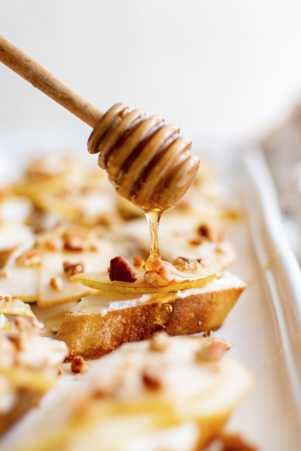 Honey dripping onto a crostini with goat cheese and pecans.