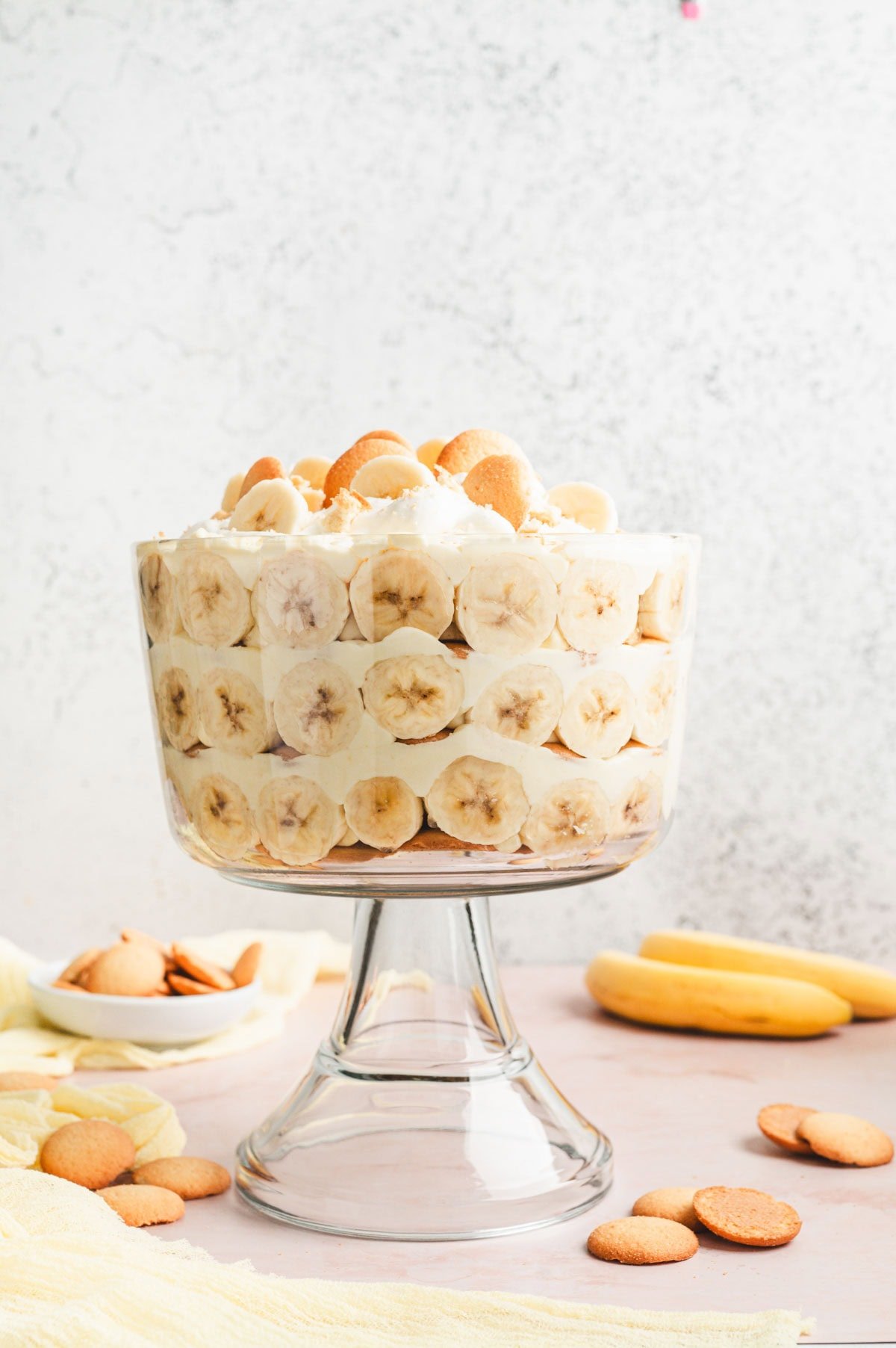 Glass trifle serving dish with layers of banana pudding, bananas, and wafers.
