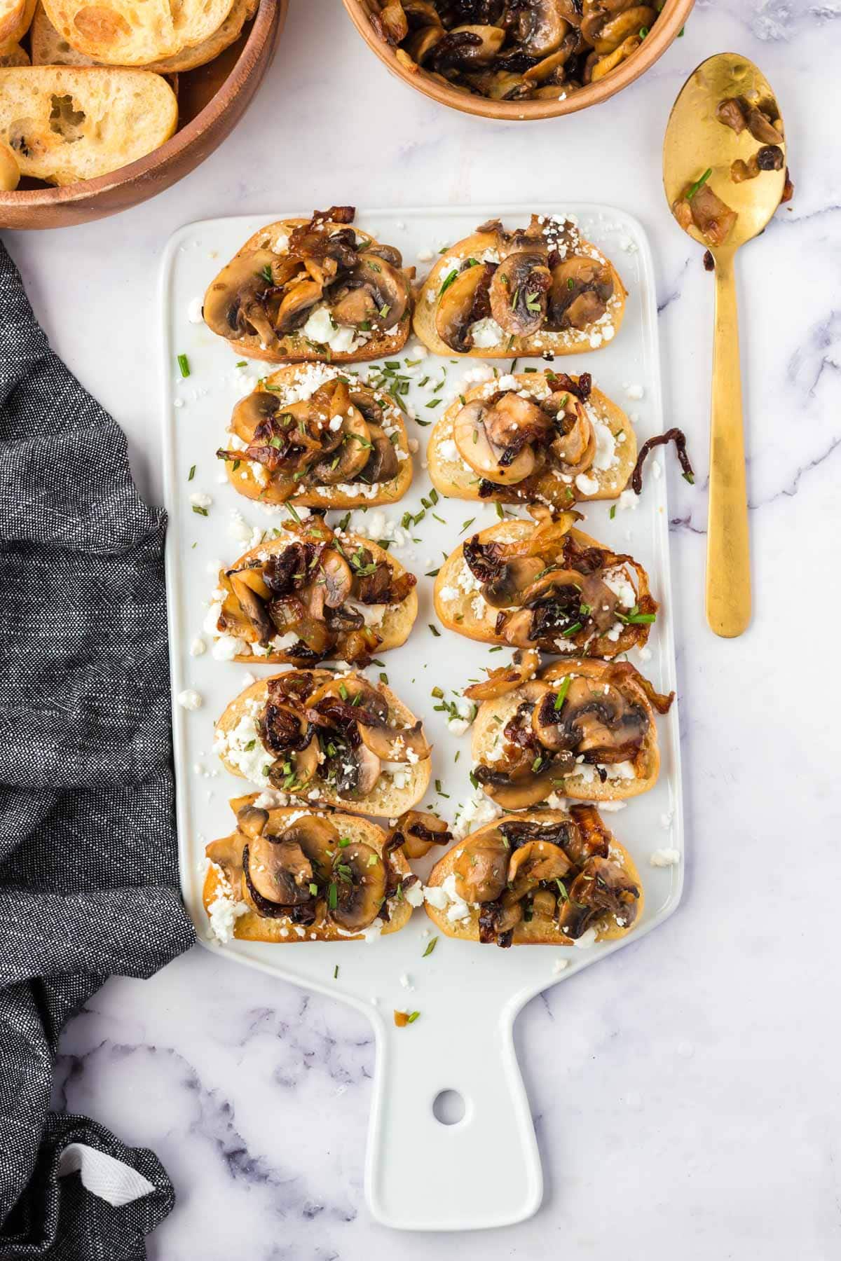 Crostini with goat cheese and mushrooms on a white cutting board.