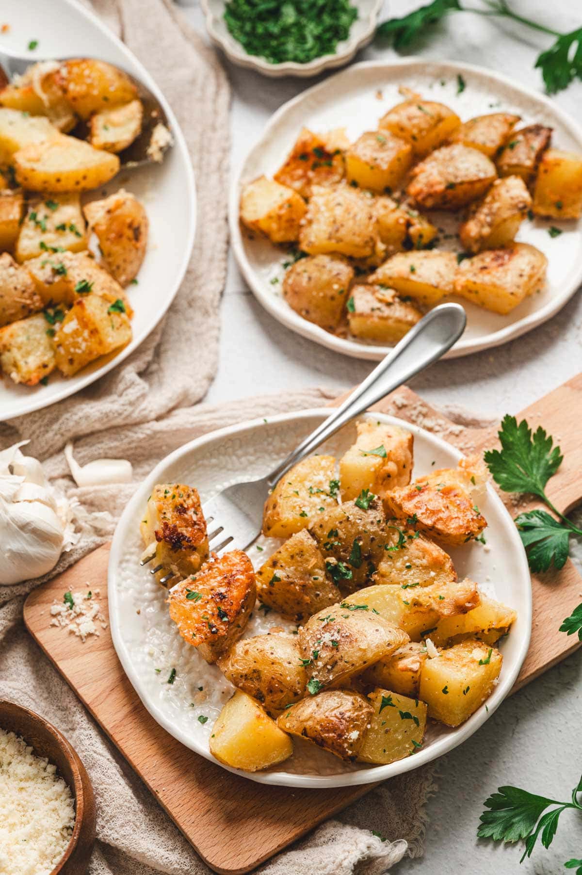 Roasted parmesan garlic potatoes on white plates, garnished with parsley.