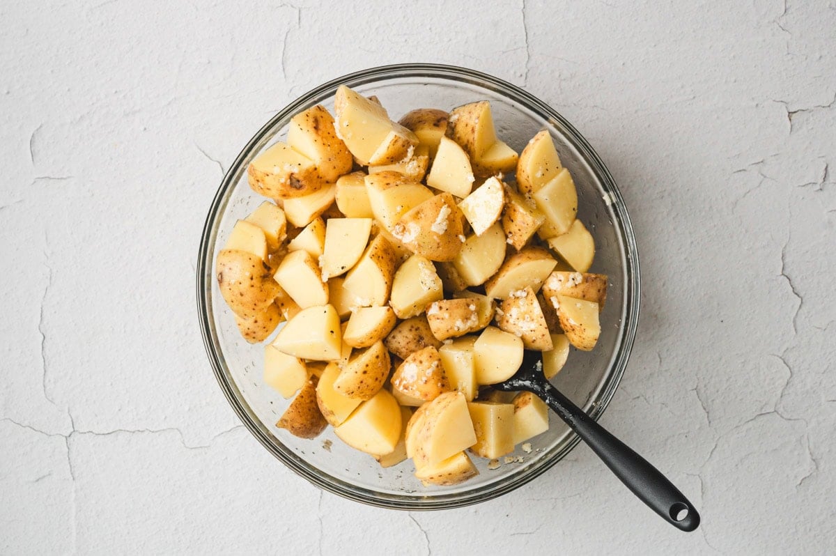 Diced raw potatoes mixed with garlic in a glass bowl.
