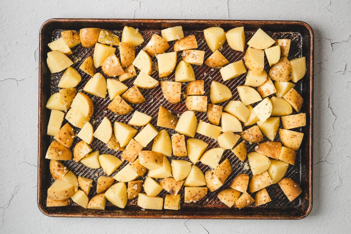 Diced raw potatoes with garlic on a sheet pan.
