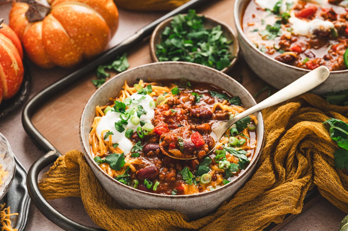 Bowl with a spoon filled with pumpkin chili topped with cheese, sour cream, green onion and cilantro.