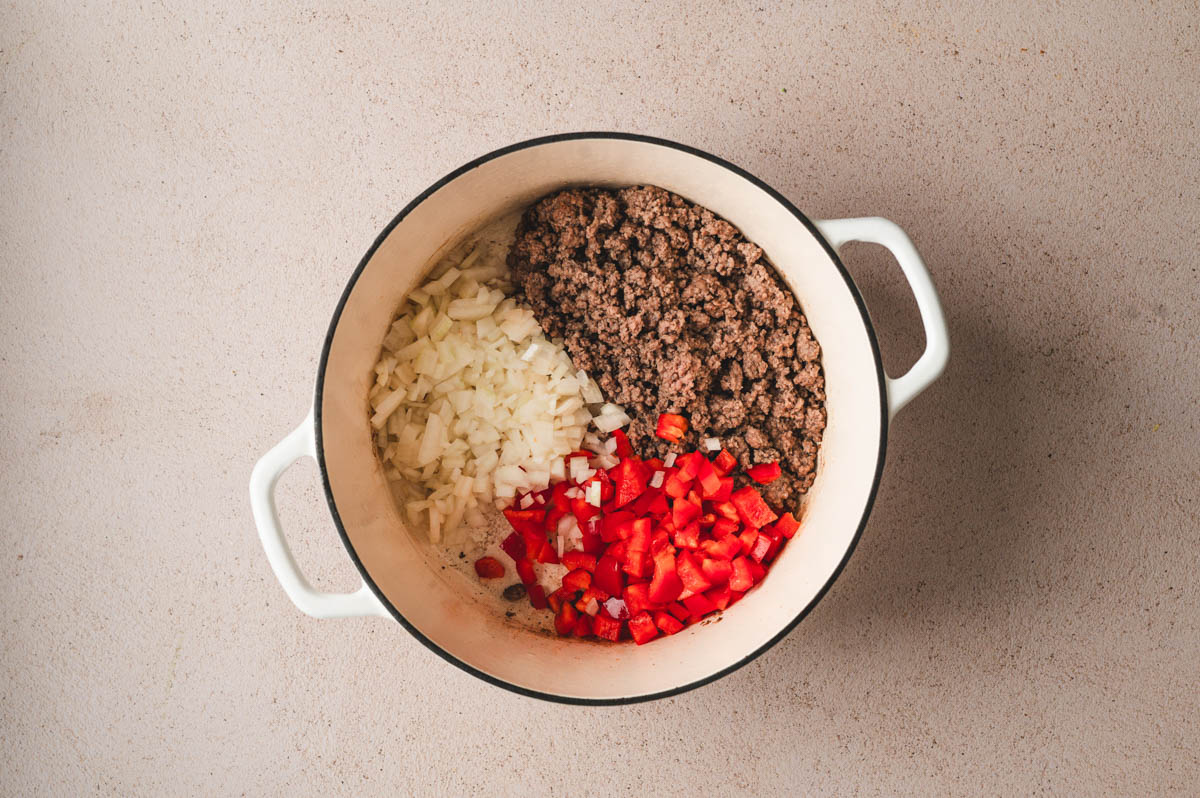 Ground beef and veggies being sauteed in a white pot.