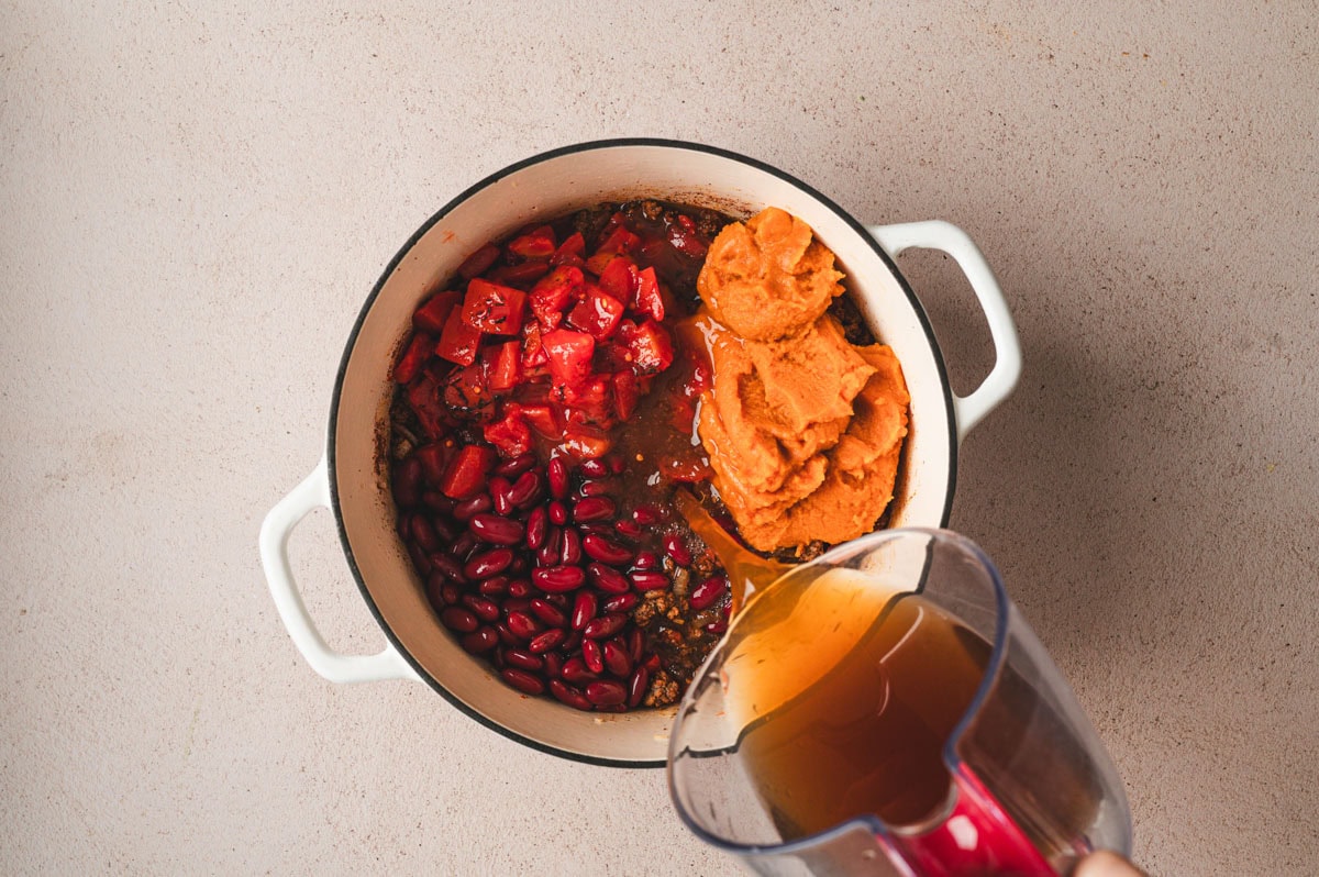 White dutch oven with meat and veggies plus kidney beans, fire roasted tomatoes, pumpkin puree and beef broth.