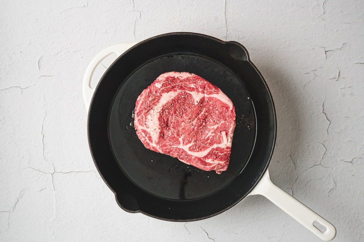 Uncooked ribeye steak on a cast iron pan.