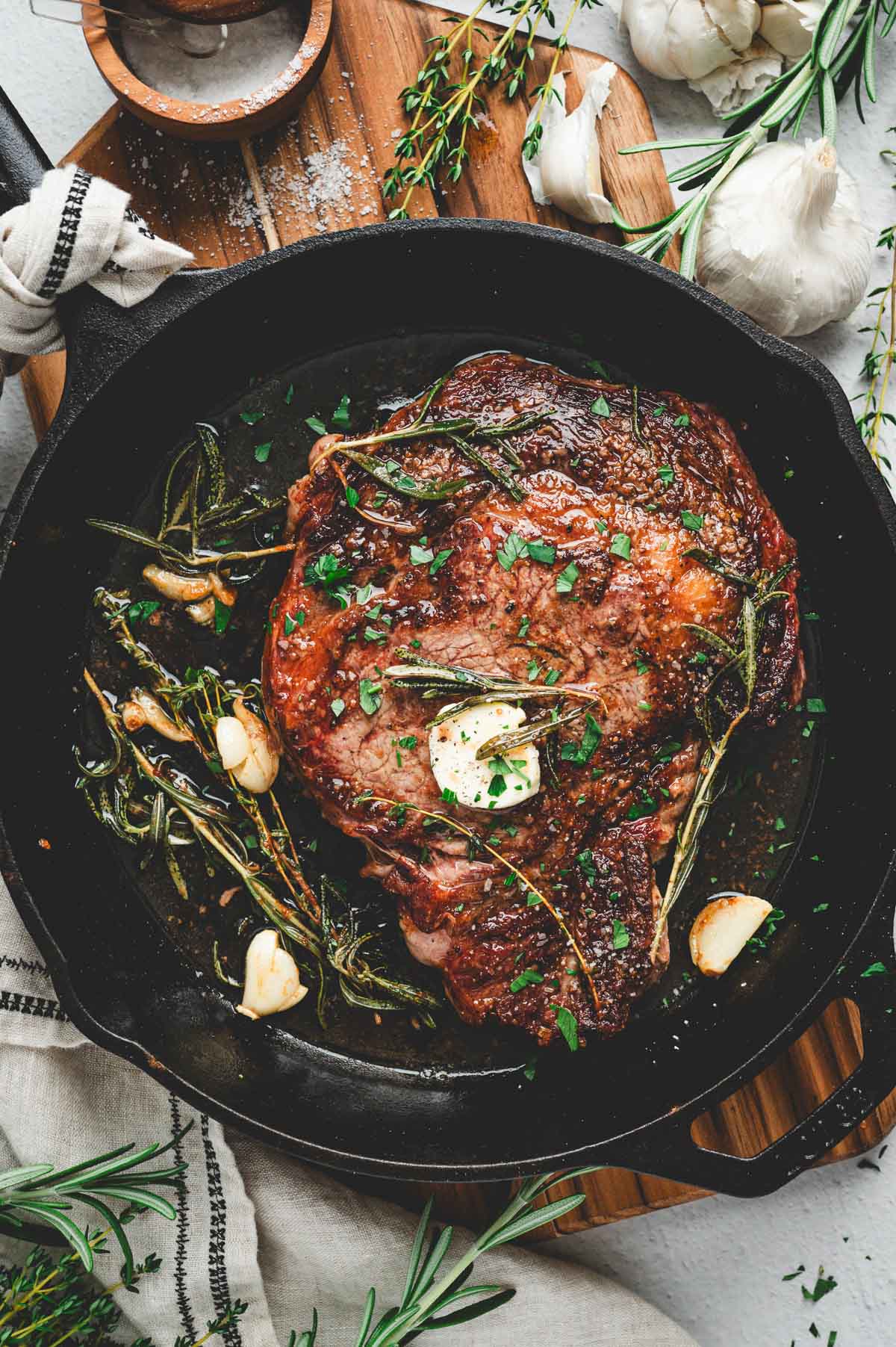 Pan seared ribeye steak on a cast iron pan with herbs, garlic, and butter.