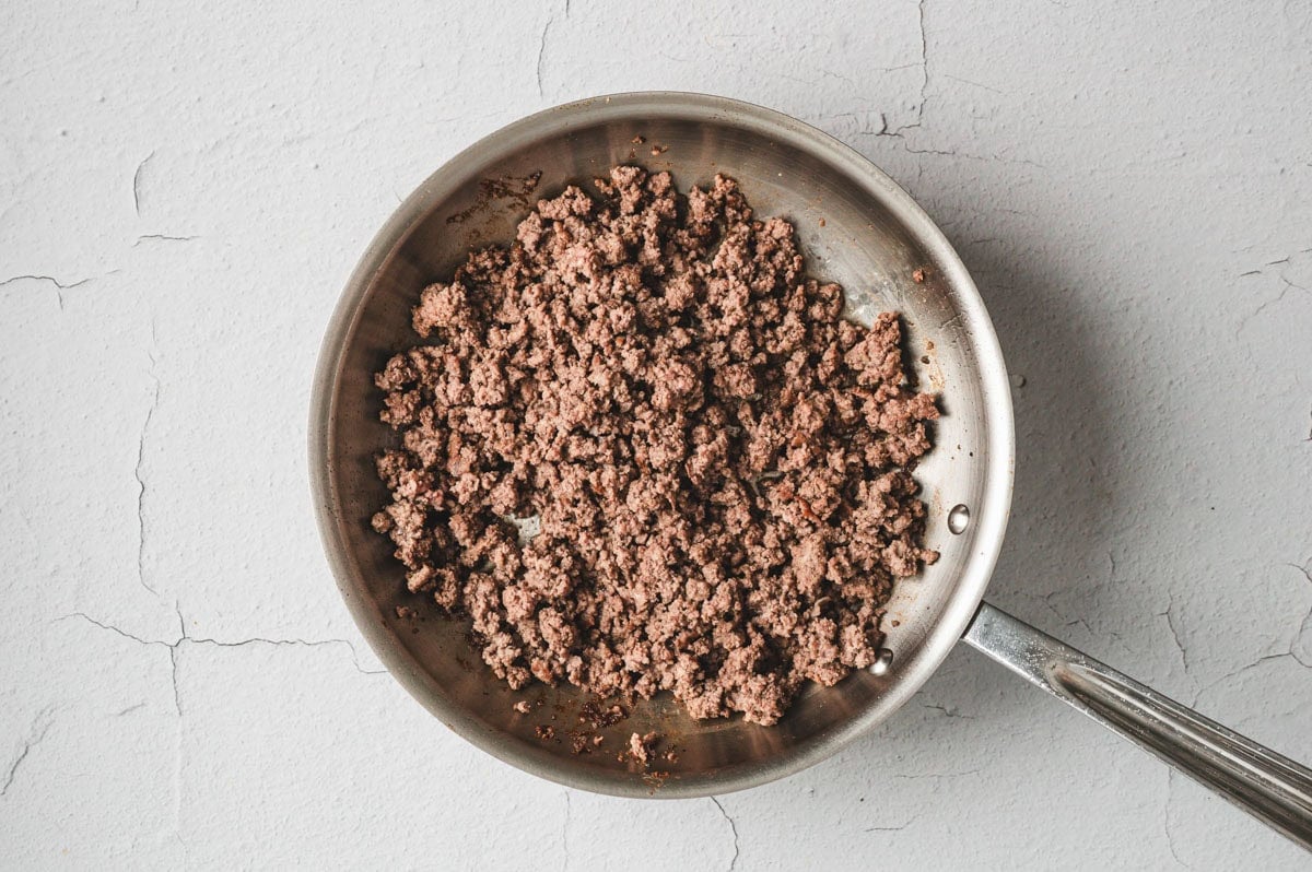 Browned ground beef in a stainless steel skillet.