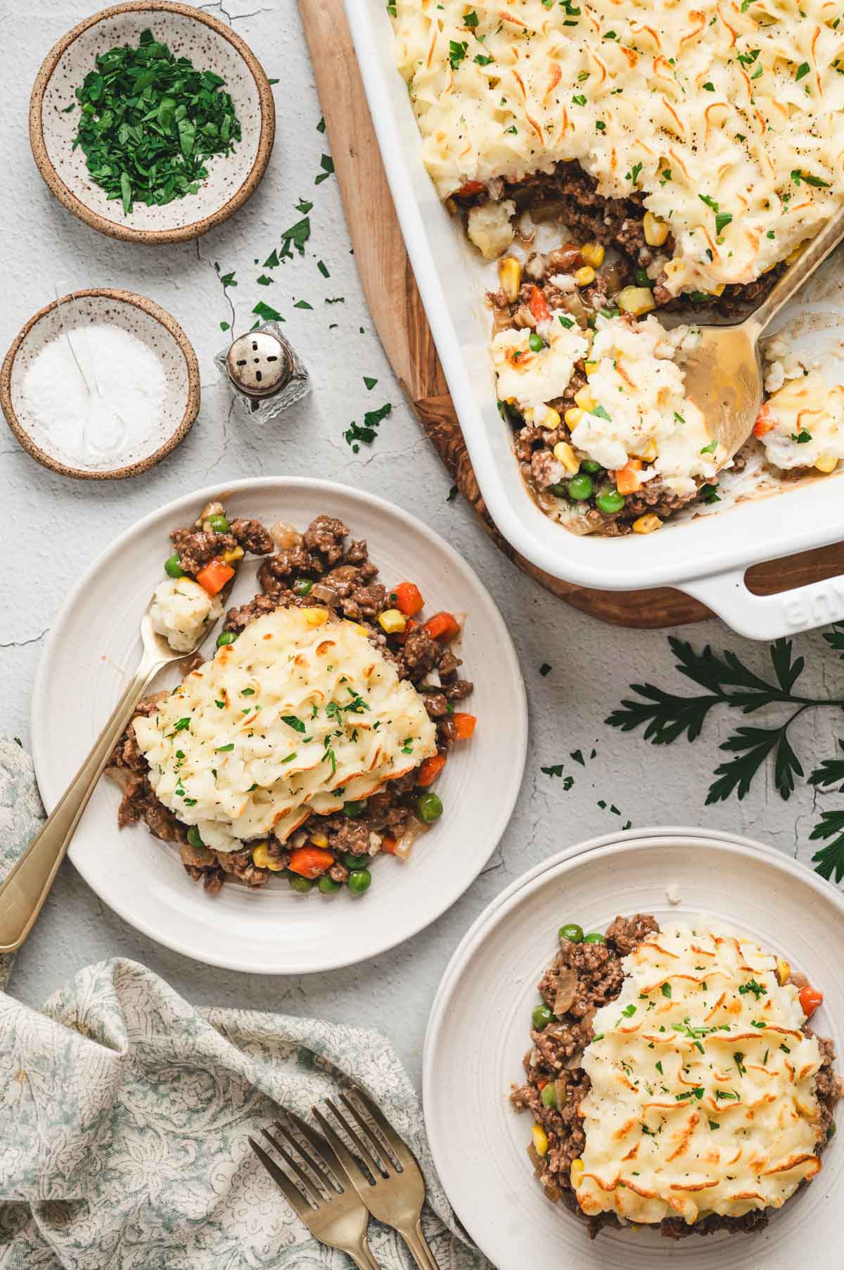 White casserole dish with shepherd's pie and two white plates with pieces of shepherd's pie.
