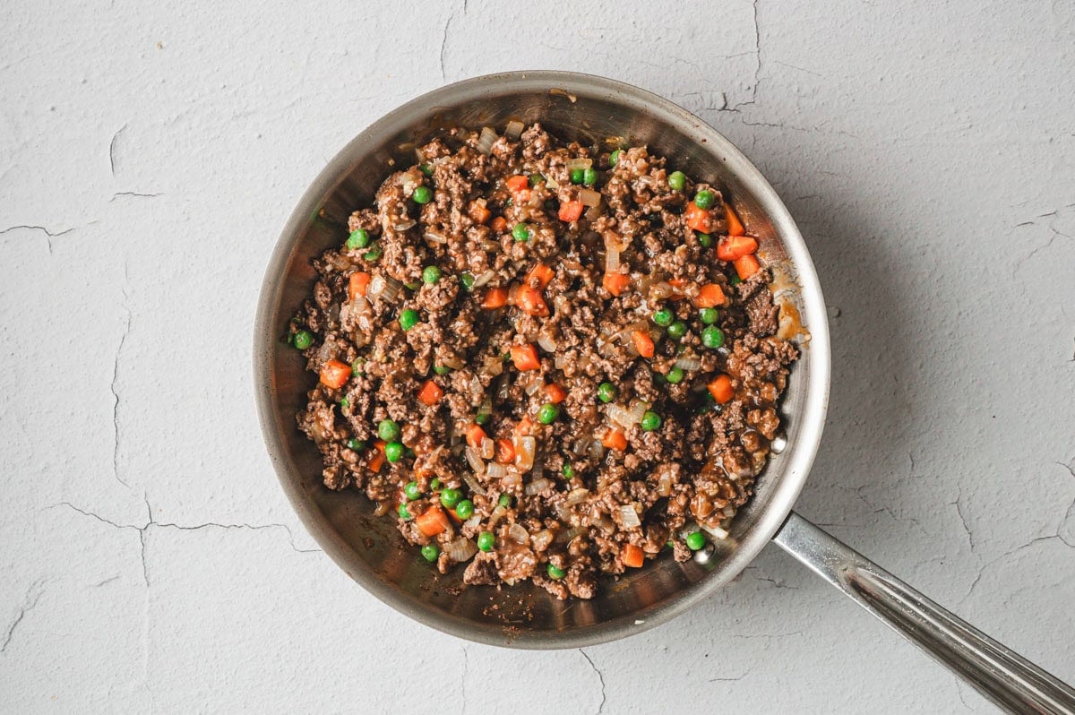Browned ground beef and vegetables in a stainless steel skillet.