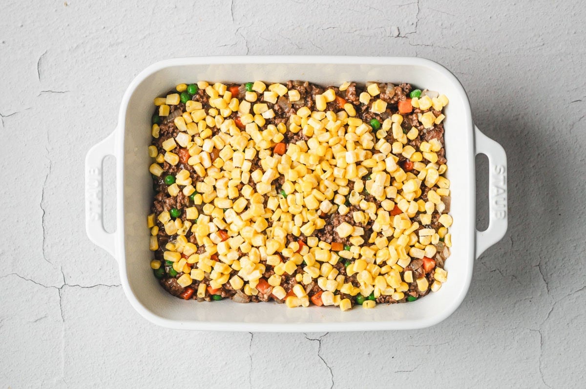 Ground beef, vegetables, corn in a white casserole dish.