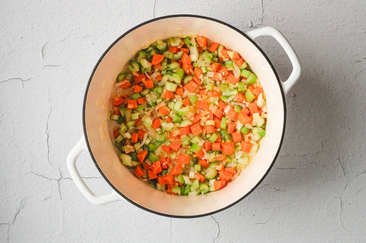 Onion, celery, and carrots sauteing in a white pot.