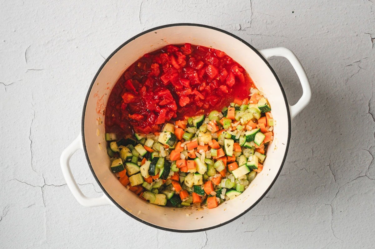 Canned tomatoed added to sauteed veggies in a white pot.