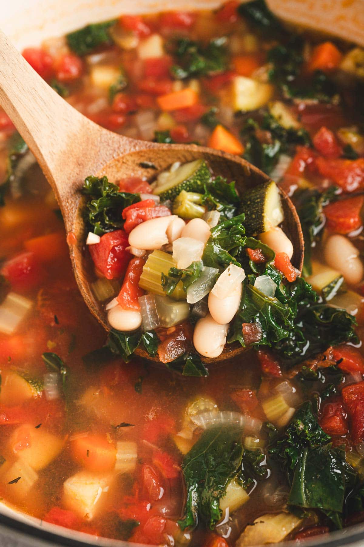 Wooden serving spoon loaded with Tuscan Vegetable Soup and beans.