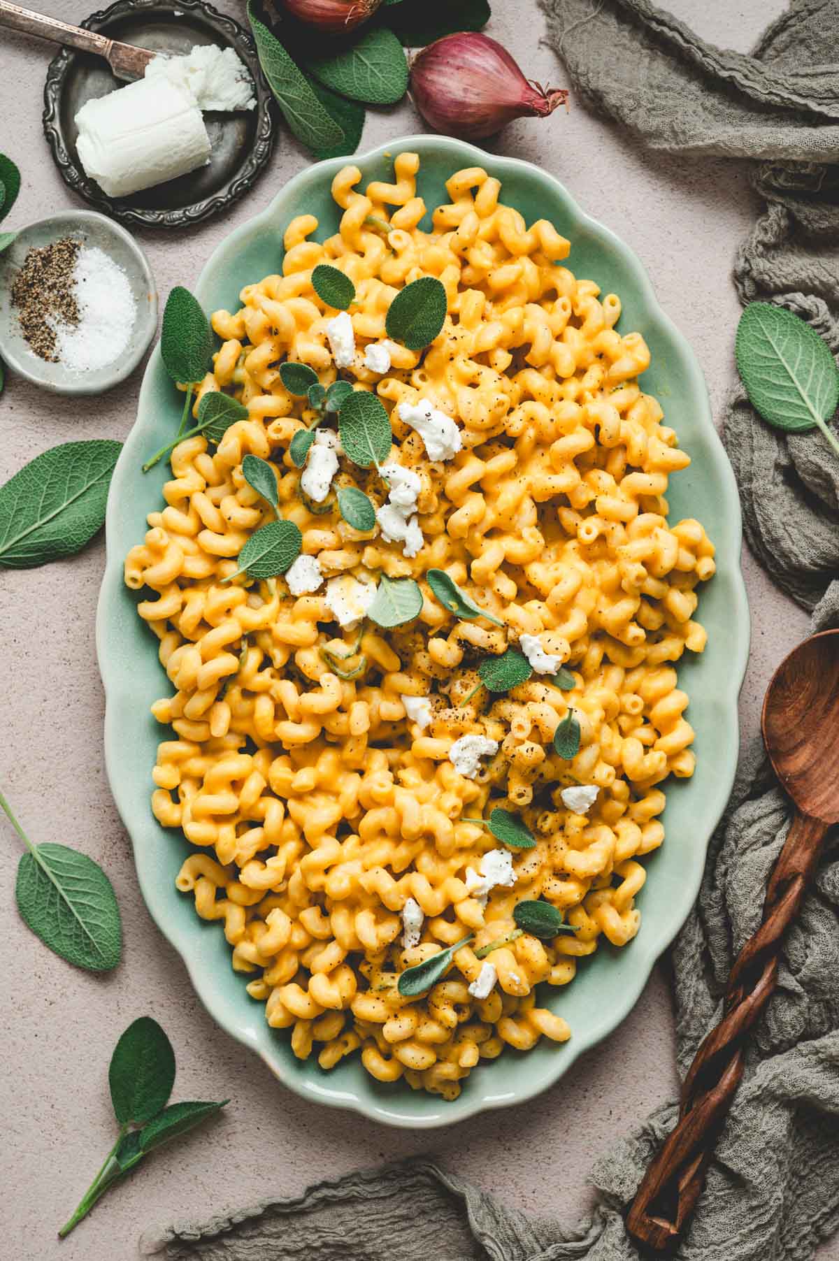 Butternut squash pasta in a light blue serving dish garnished with goat cheese, sage leaves, and black pepper.