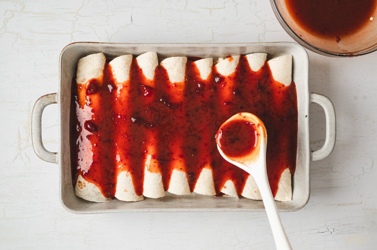 Cranberry enchilada sauce being poured over enchiladas.