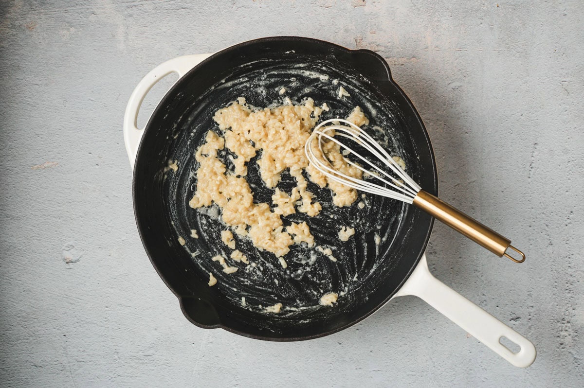Butter and flour in a saucepan being stirred with a whisk.