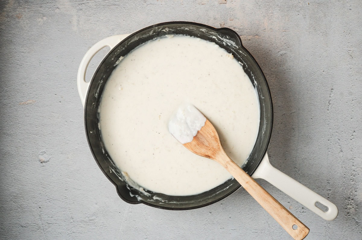 Cream sauce in a saucepan with a wooden spatula.