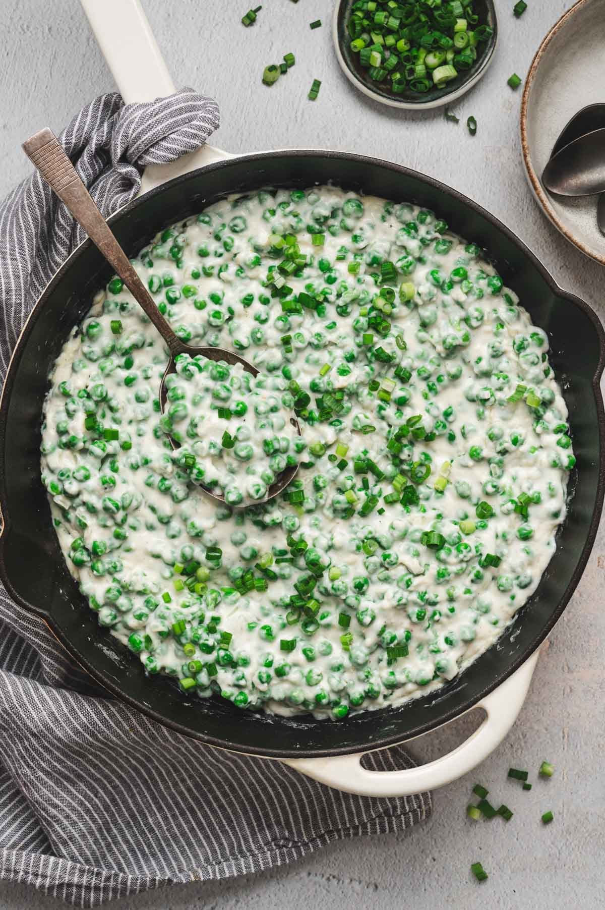 Creamed peas in a saucepan garnished with green onions and pepper.