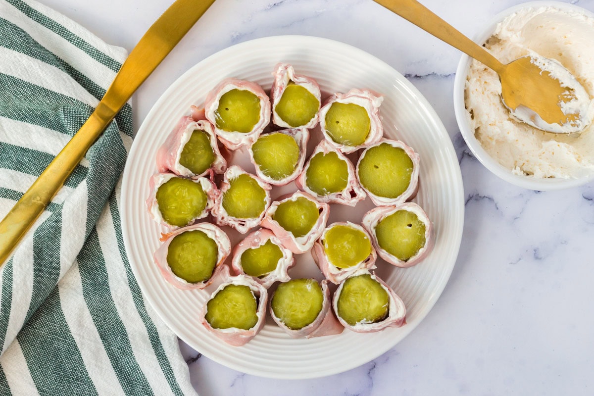 Ham and pickle roll ups sliced into pieces on a white plate.