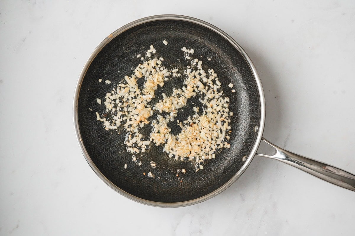 Onions and garlic being sauteed in a skillet.