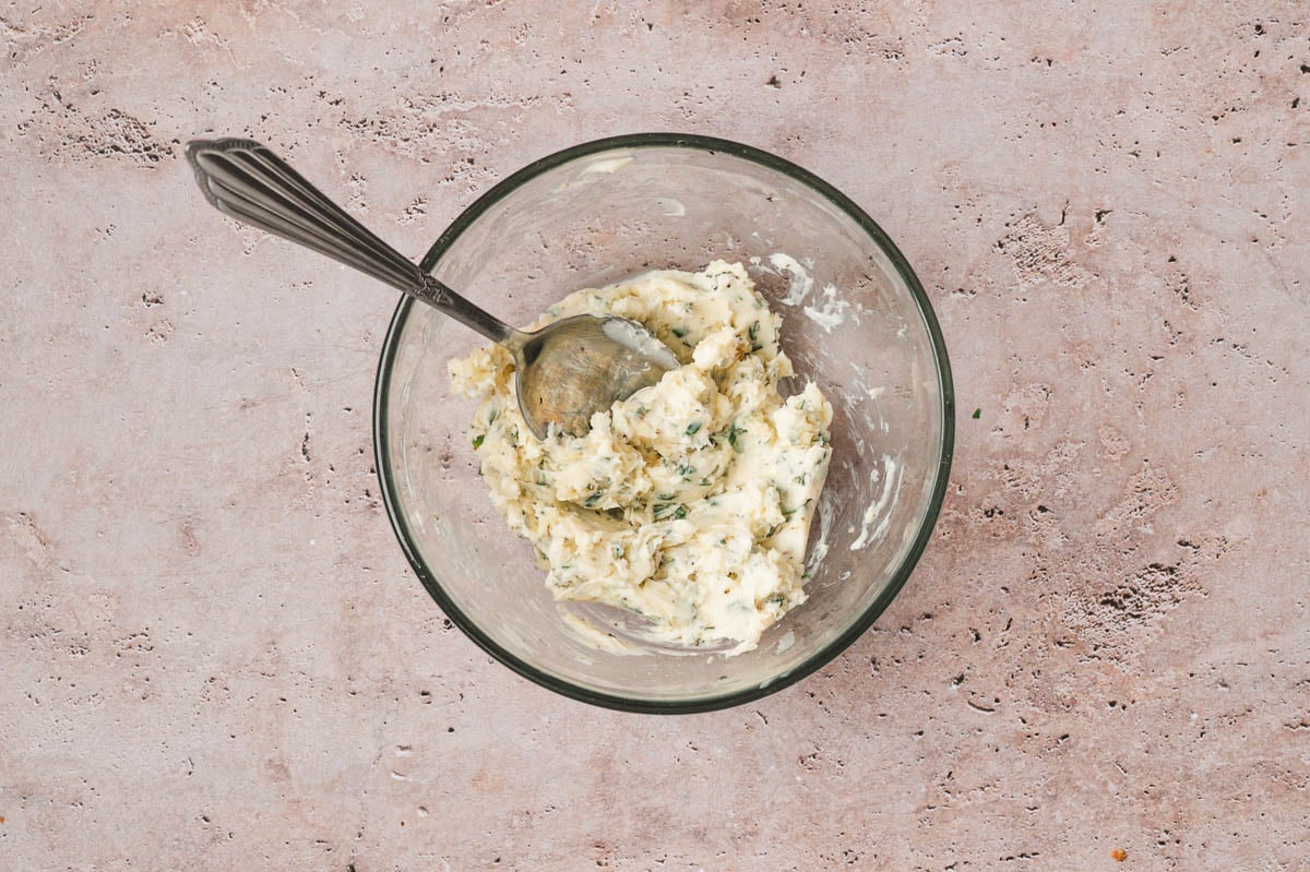 Herbs and butter in a glass bowl with spoon.