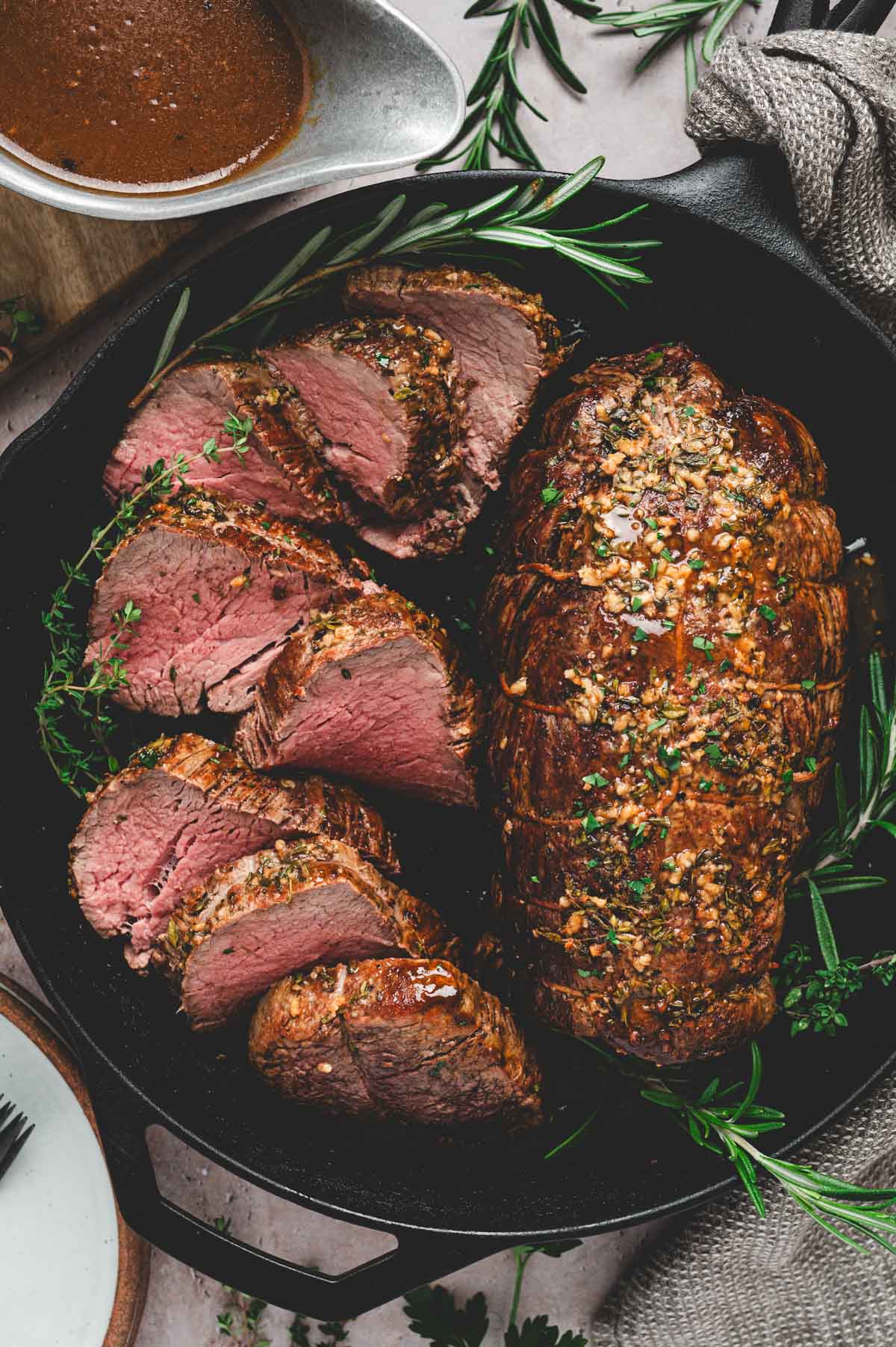 Cooked beef tenderloin roast in a cast iron pan with seasoning and herbs.