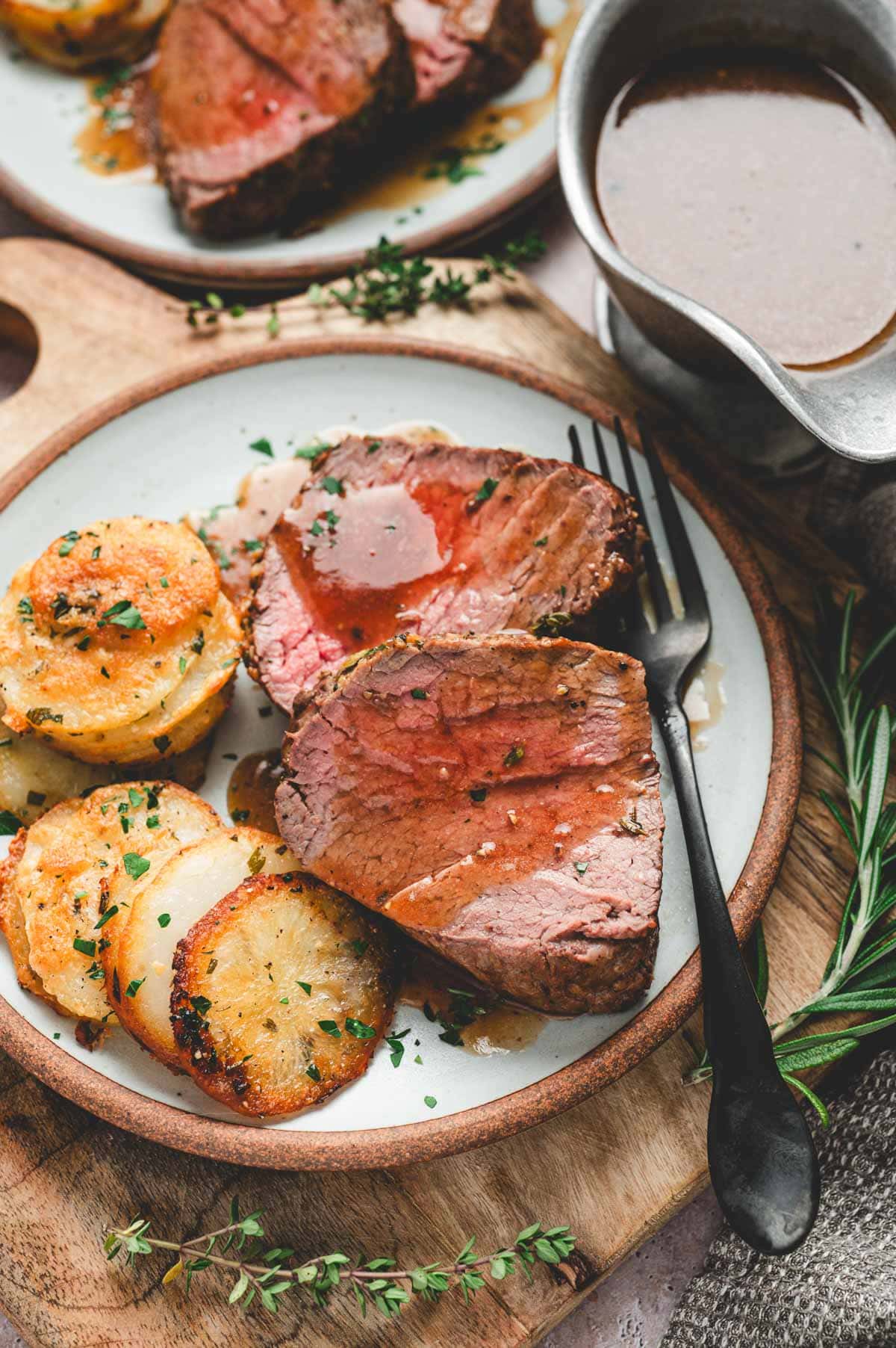 Slices of beef tenderloin on a plate next to potato stacks.