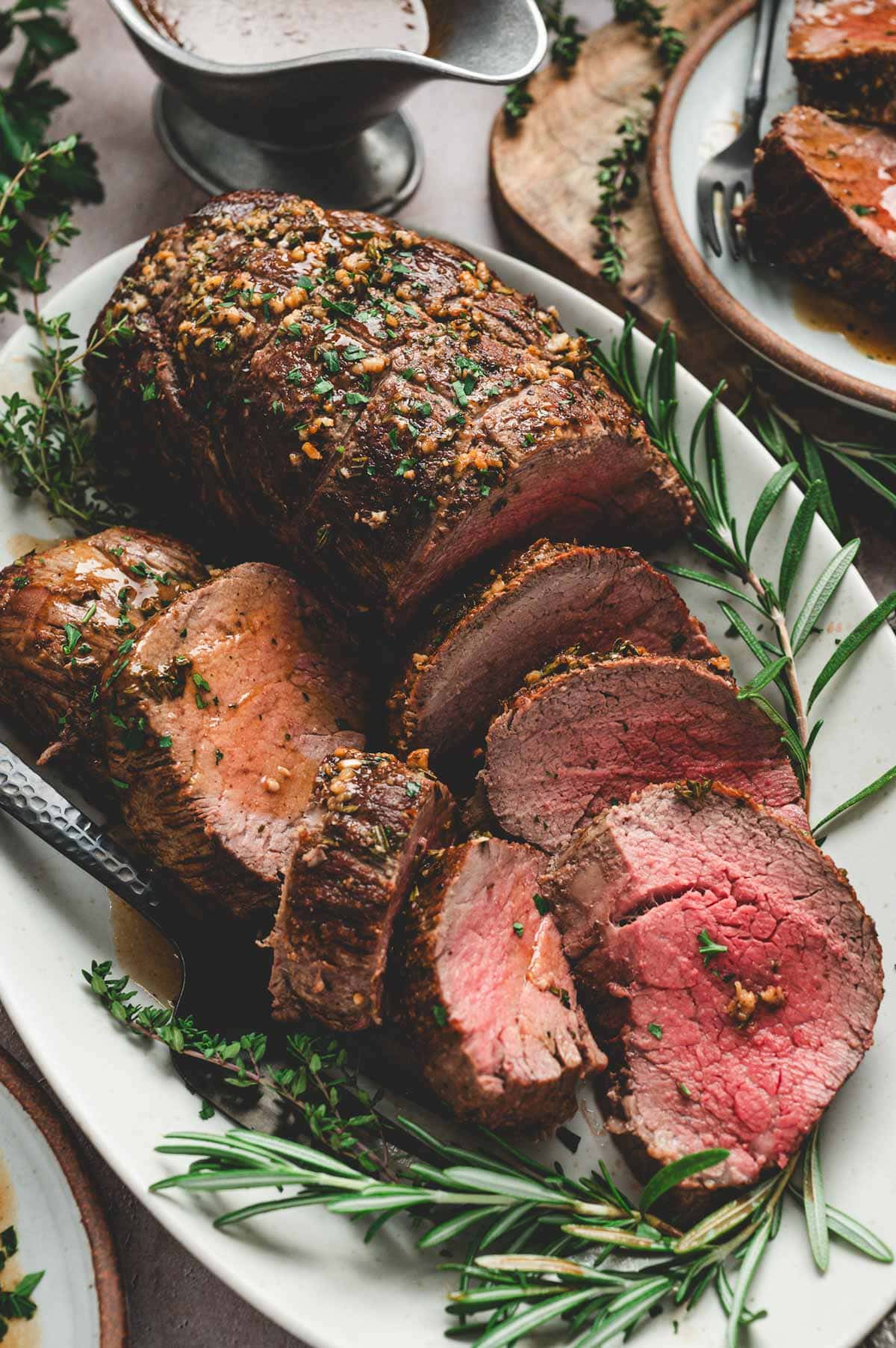 Beef tenderloin roast on a serving platter with fresh herbs and serving fork.