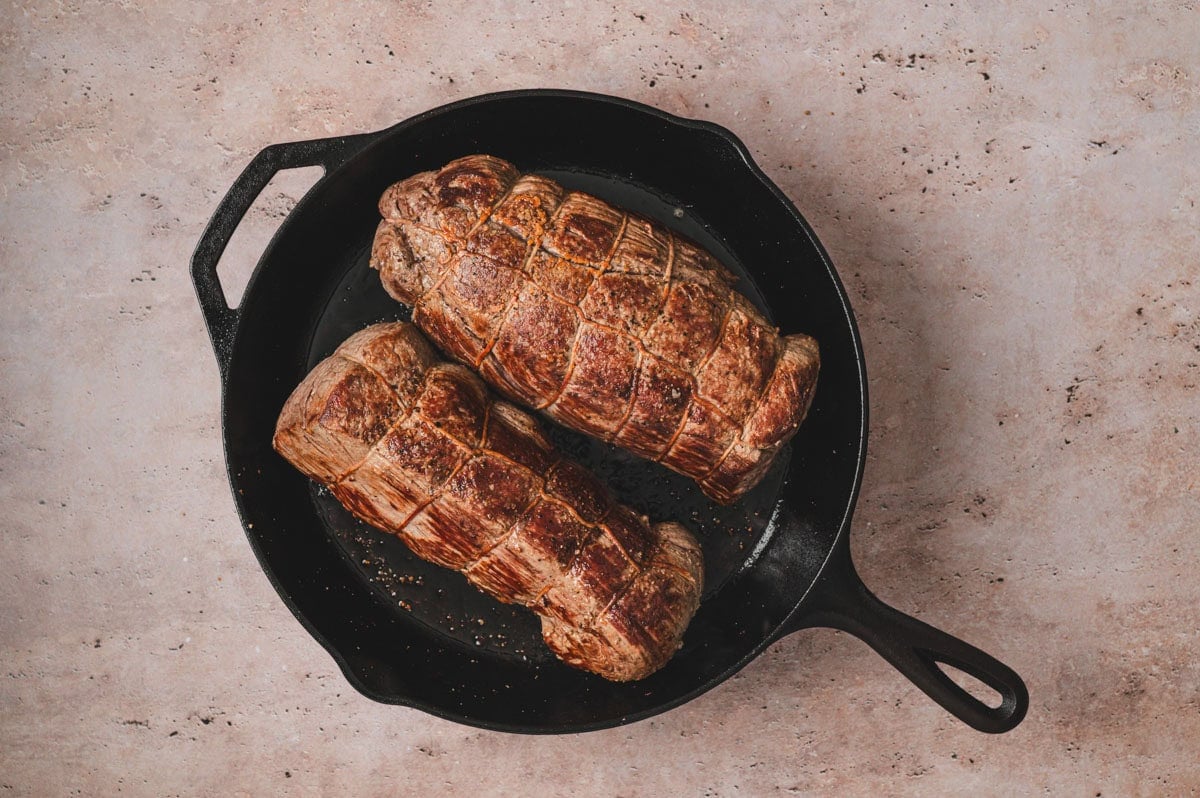 Seared beef tenderloin roasts tied, in a cast iron pan.