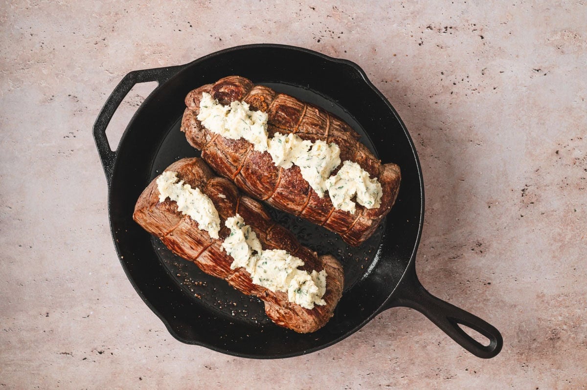 Seared beef tenderloin roasts in a cast iron pan with herb butter on top.