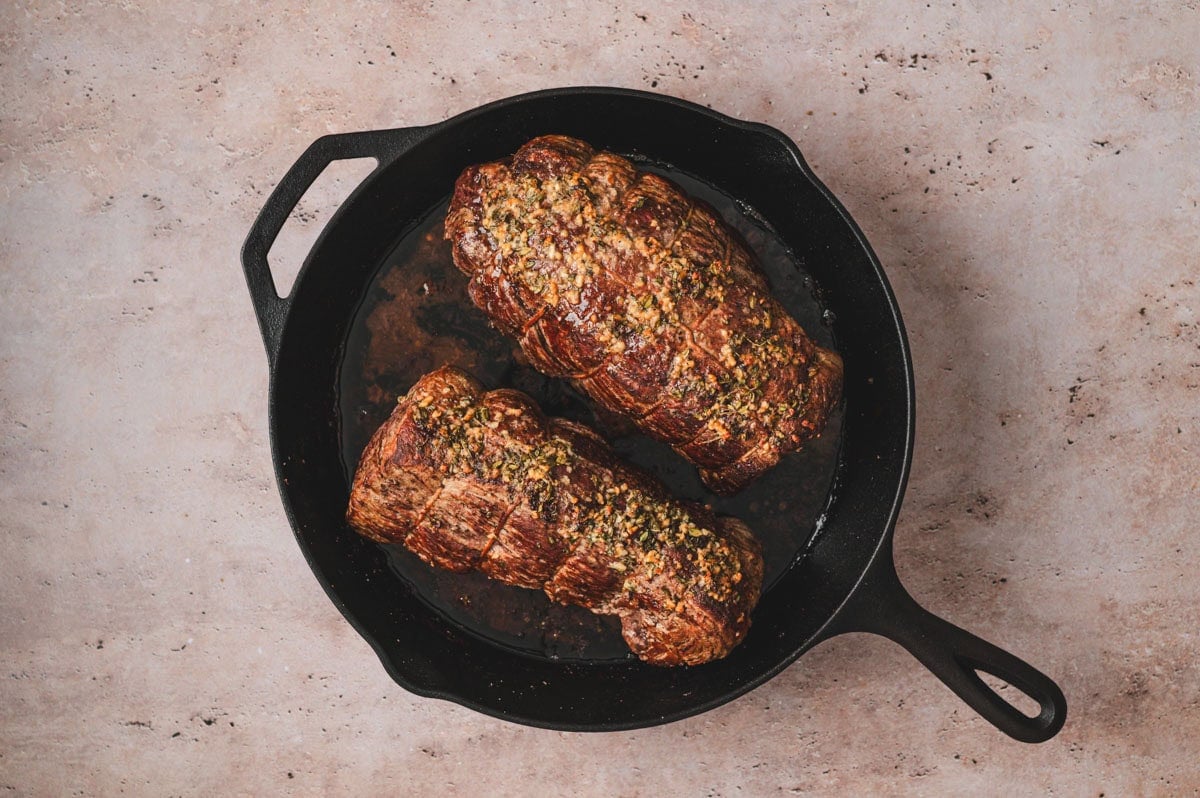 Seared, cooked beef tenderloin roast in a cast iron pan.