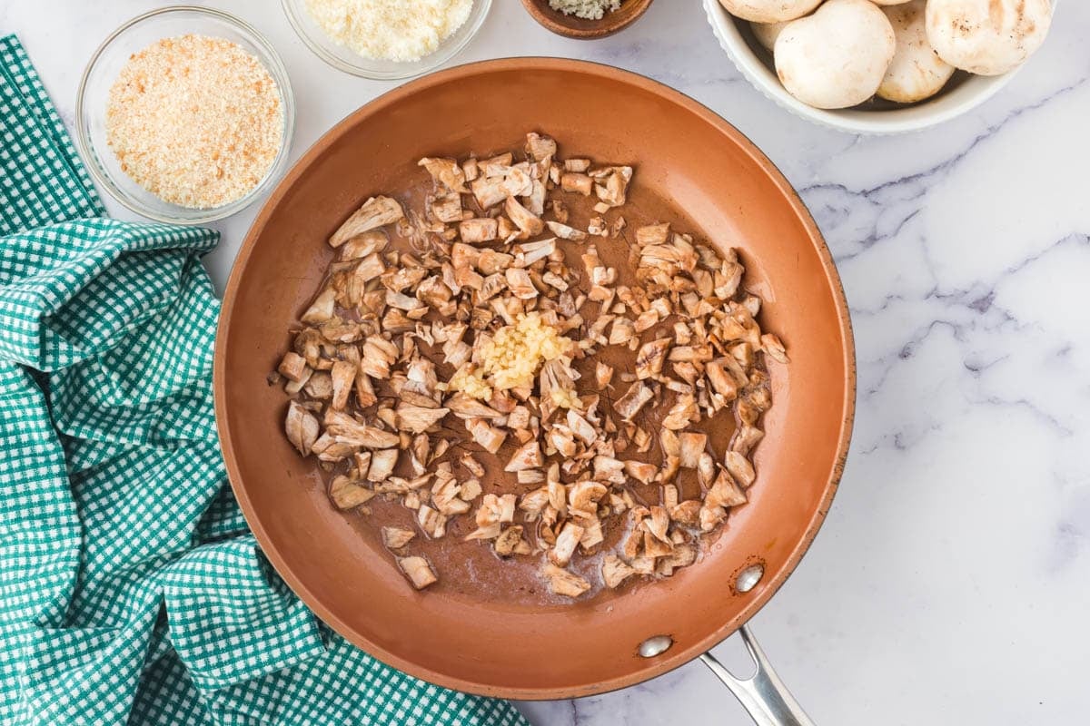Sautéing chopped mushrooms and garlic in a pan.